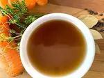 naturally gluten-free beef bone broth in a white bowl with carrots, bay leaves and peppercorns.