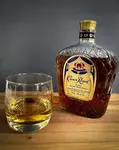 A bottle of Crown Royal on a wooded board with a poured crystal glass