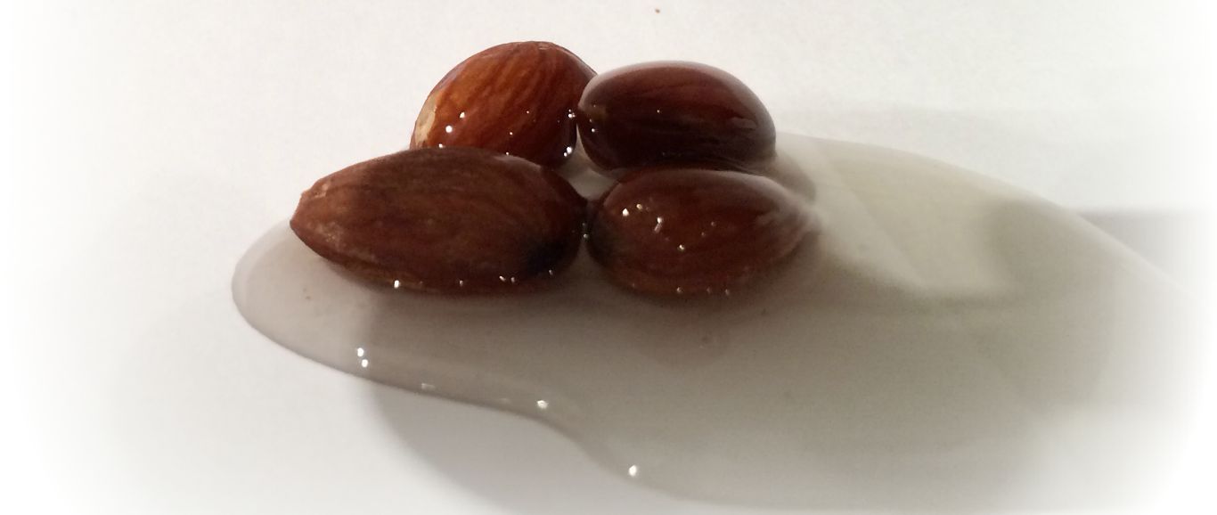 Four almonds drizzled with almond oil on a white background.