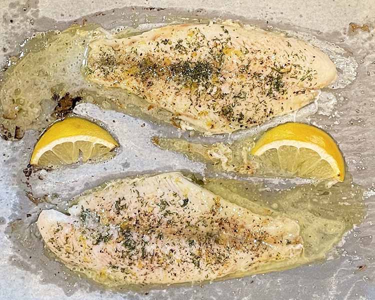 2 baked whitefish filets on parchment with lemon wedges 2 baked whitefish filets on parchment with lemon wedges