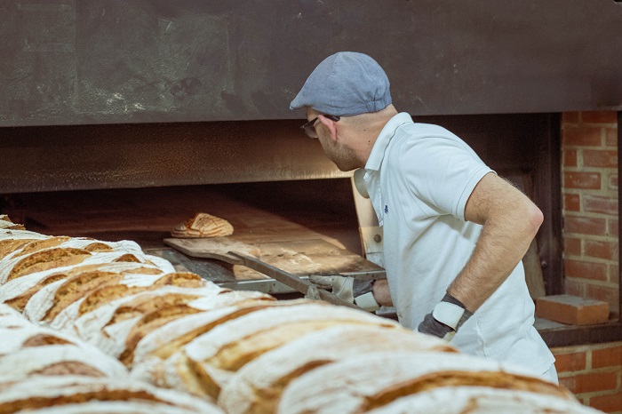 baker taking artisan bread out of a large oven