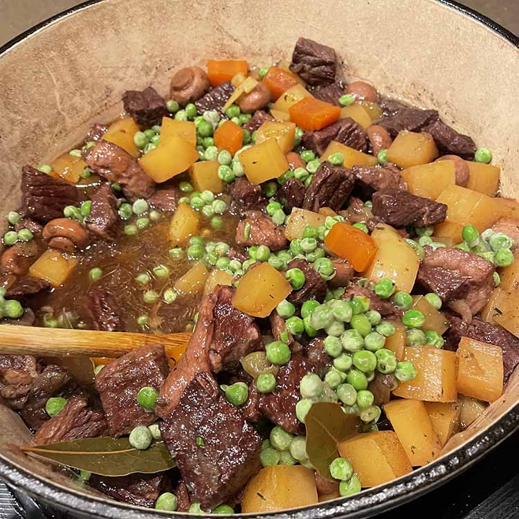 beef stew in Dutch oven with potatoes, carrots, bay leaves and green peas. beef stew in Dutch oven with potatoes, carrots, bay leaves and green peas.