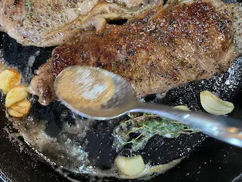 butter bastig a sirloin steak in a cast iron pan with garlic and thyme.