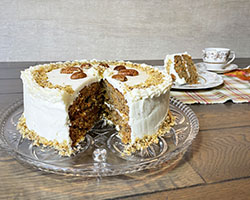 Whole carrot cake with slice out.  Slice and teacup in background.