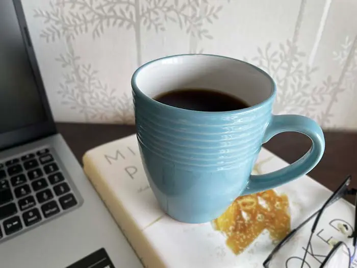 Coffee mug sitting on a book.  Laptop to left side. Glasses bottom right corner. Coffee mug sitting on a book.  Laptop to left side. Glasses bottom right corner.