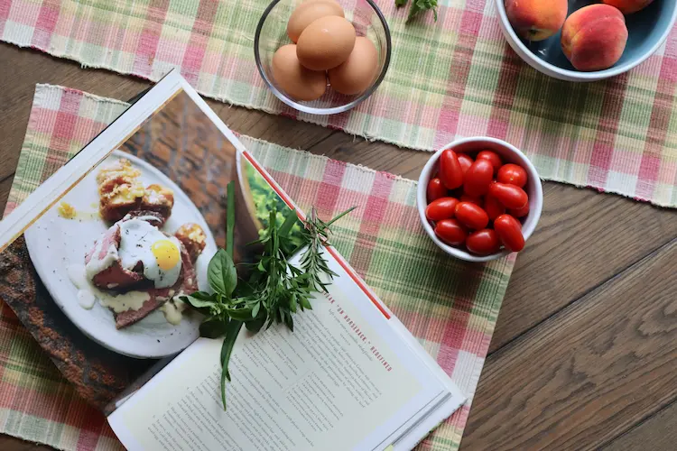 overhead shot of open cookbook with herbs, eggs, peaches and tomatoes overhead shot of open cookbook with herbs, eggs, peaches and tomatoes