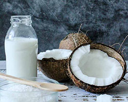 split coconut with a bottle of coconut milk and a wooden spoon.