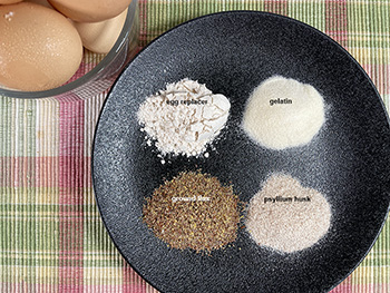 egg substitutes on black plate. Commercial eggs replacer, gelatin, psyllium husk, ground flax egg substitutes on black plate. Commercial eggs replacer, gelatin, psyllium husk, ground flax