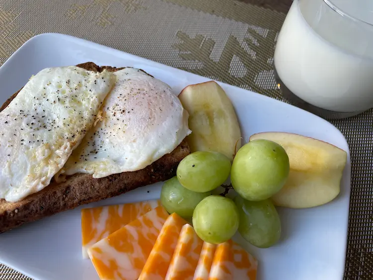 eggs over easy on toast with cheese, grapes, apples and a glass of milk