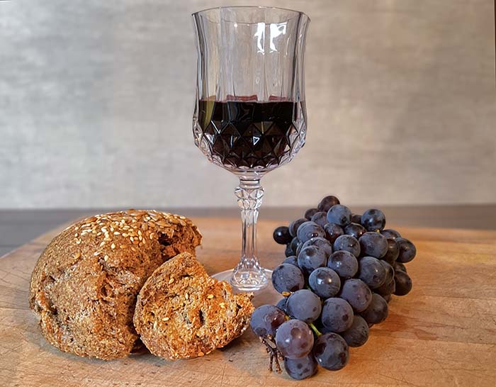 crystal stemmed wine glass with red wine. Broken loaf of flax bread and blue grapes at the base. crystal stemmed wine glass with red wine. Broken loaf of flax bread and blue grapes at the base.