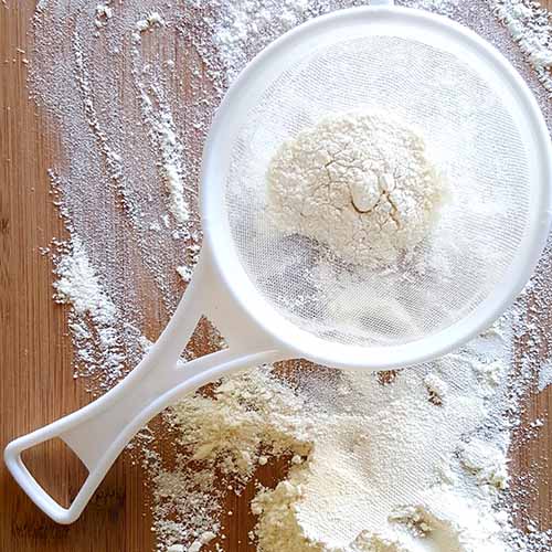 white flour in a sieve and spread beautifully over and wooden cutting board.