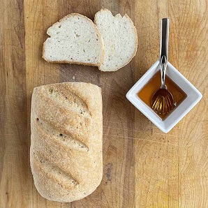 loaf of gluten-free bread with two slices and a square dish with honey and a spoon.