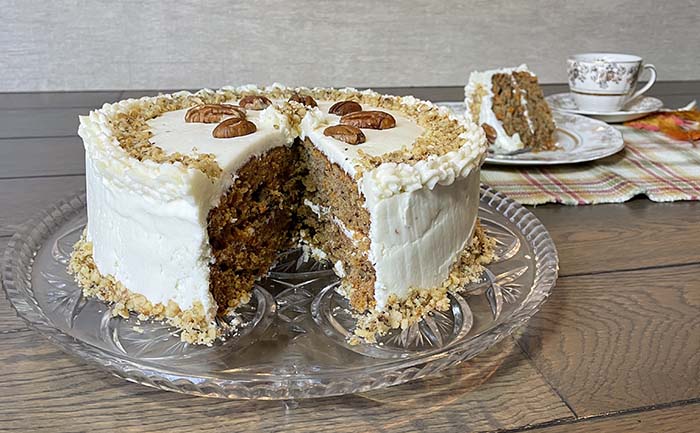 gluten-free carrot cake. Whole frosted carrot cake in foreground.  Slice of cake and tea cup in background.