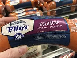 pillar's kolbassa hand held with supermarket shelf in backgournd