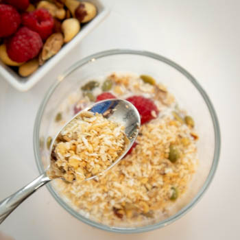 overhead shot of granola cereal in milk beside a bowl of nuts and berries
