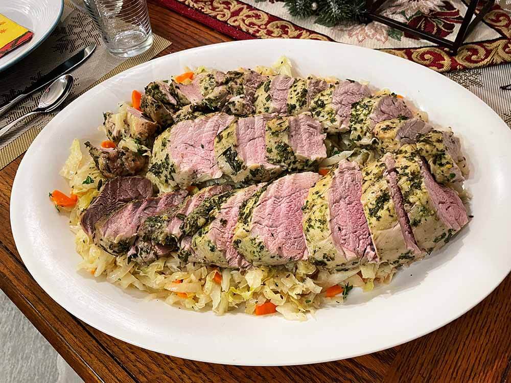 herbed pork tenderloin on a bed of warm cabbage salad served on a white platter.