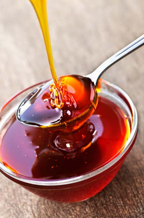 pouring honey into a spoon over a small glass bowl full of honey.