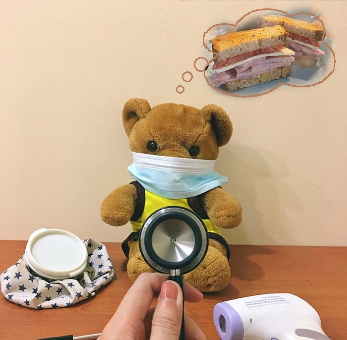 teddy bear wearing surgical mask. ice bag on left side, hand holding stethoscope in foreground and electronic thermometer to left. teddy bear wearing surgical mask. ice bag on left side, hand holding stethoscope in foreground and electronic thermometer to left.