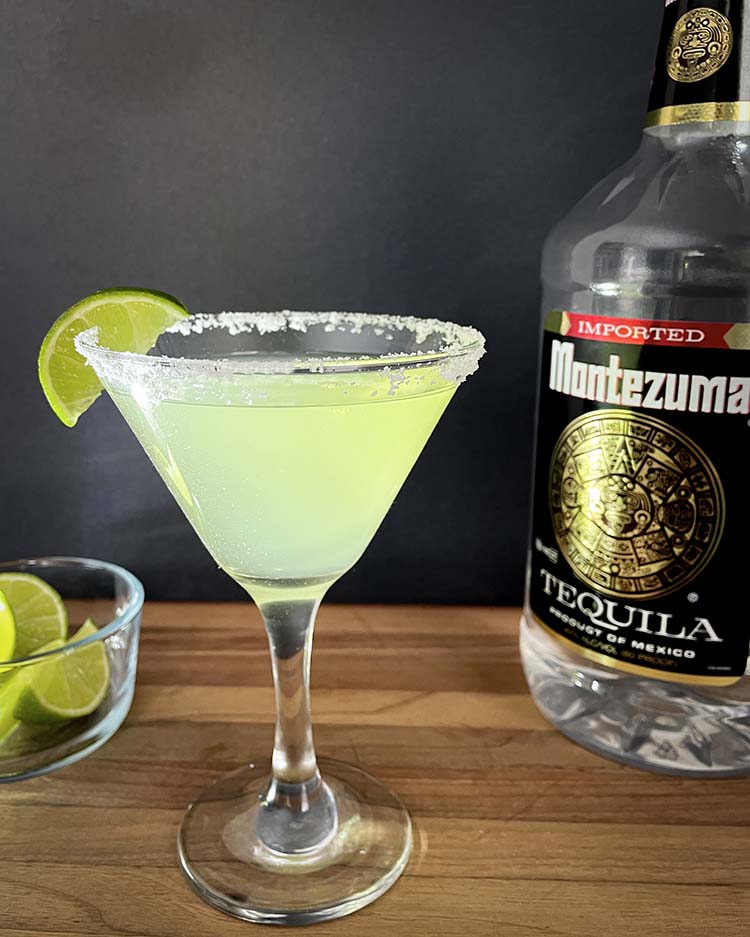 margarita in a martini glass with lime beside tequila bottle