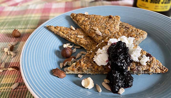 Four triangular pieces of Nordic Style flatbread with goat cheese, dark jam and nuts on a teal plate. Four triangular pieces of Nordic Style flatbread with goat cheese, dark jam and nuts on a teal plate.