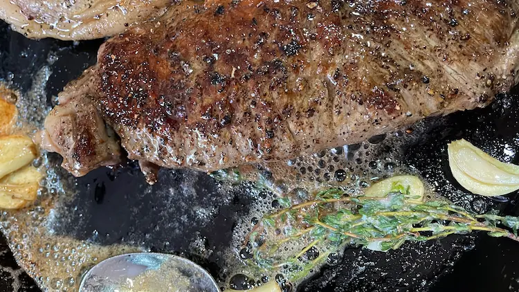 sirloin steak in frying pan with garlic and thyme