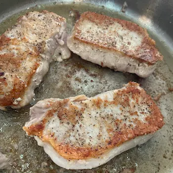 pork chops frying in pan