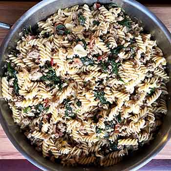 rotini in a skillet with sausage, greens and bacon