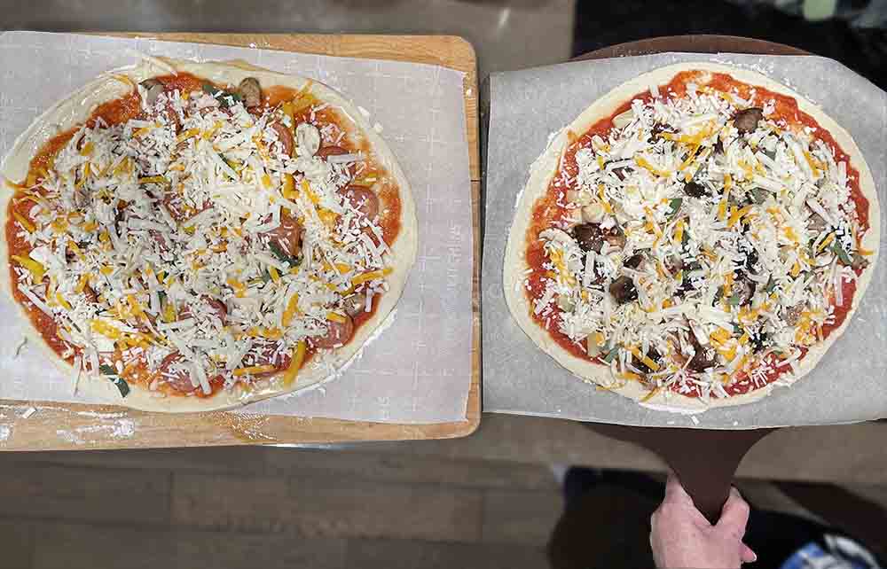 two pizzas topped and ready to go in the oven two pizzas topped and ready to go in the oven