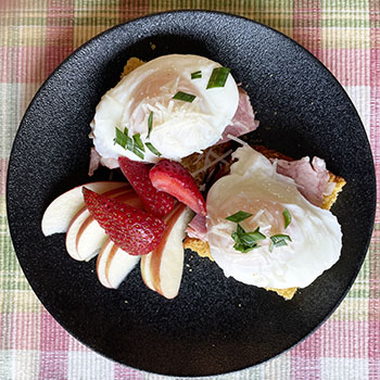 poached eggs and ham on corn bread on a black plate