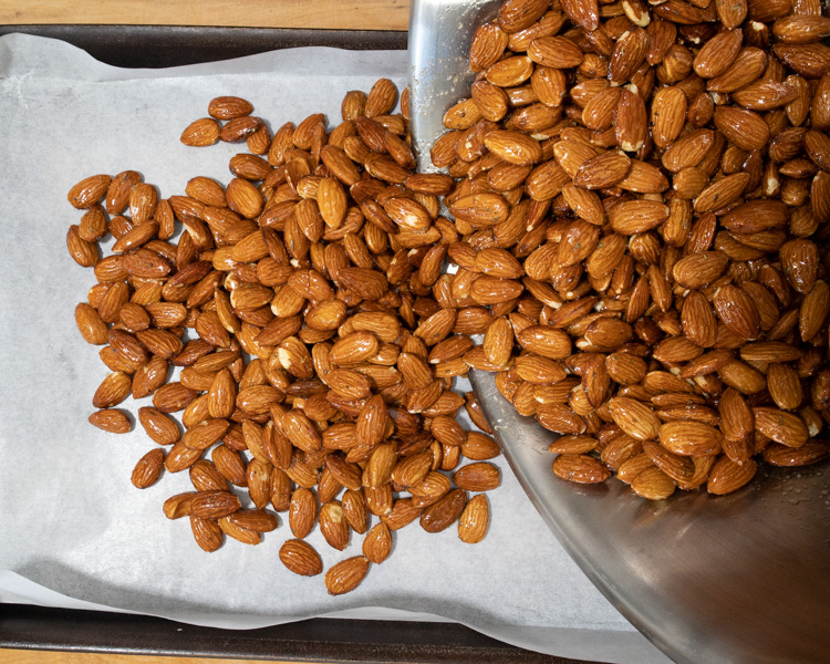 pouring seasoned almonds onto baking tray