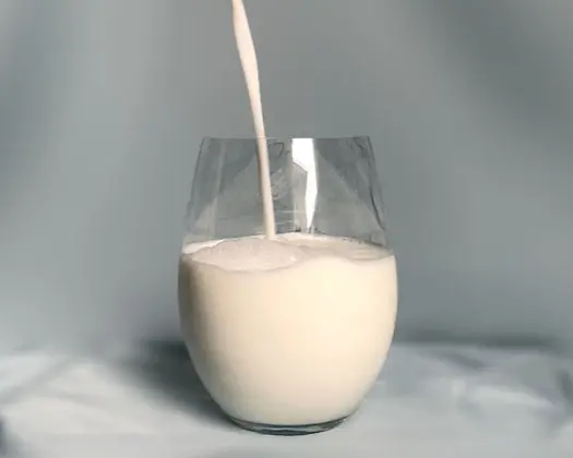 milk pouring into a glass on a grey silk background. 