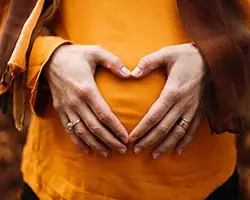 woman making heart shape over pregnant belly