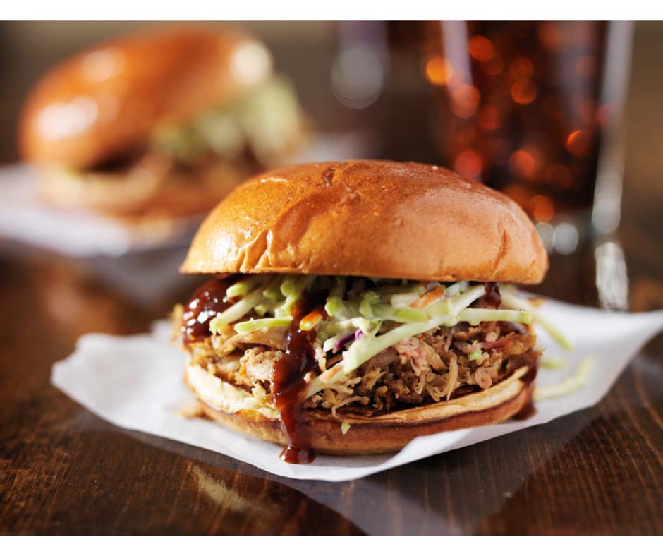 pulled pork sandwich on a bun with lettuce and barbecue sauce spilling out the side.