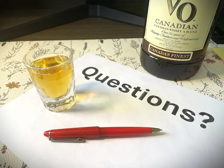 paper with the text "questions?" beside a pen and a shot glass of whisky paper with the text "questions?" beside a pen and a shot glass of whisky