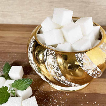 sugar cubes in a decorative bowl.  A few cubes on the side with mint leaves.