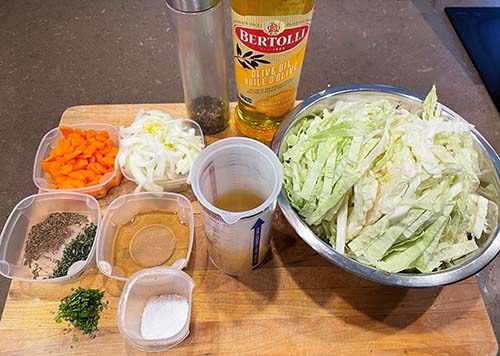 Ingredients for warm cabbage salad.  diced onion, diced carrot, garlic, honey, chicken stock, white wine vinegar, white wine, caraway seeds, fresh thyme, fresh parsley, oil, salt and pepper