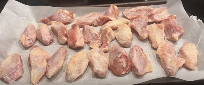 uncooked chicken wings spread on a parchment lined baking sheet. uncooked chicken wings spread on a parchment lined baking sheet.