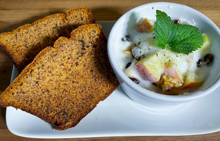 Sliced gluten free banana bread on plate with a bowl of fruit